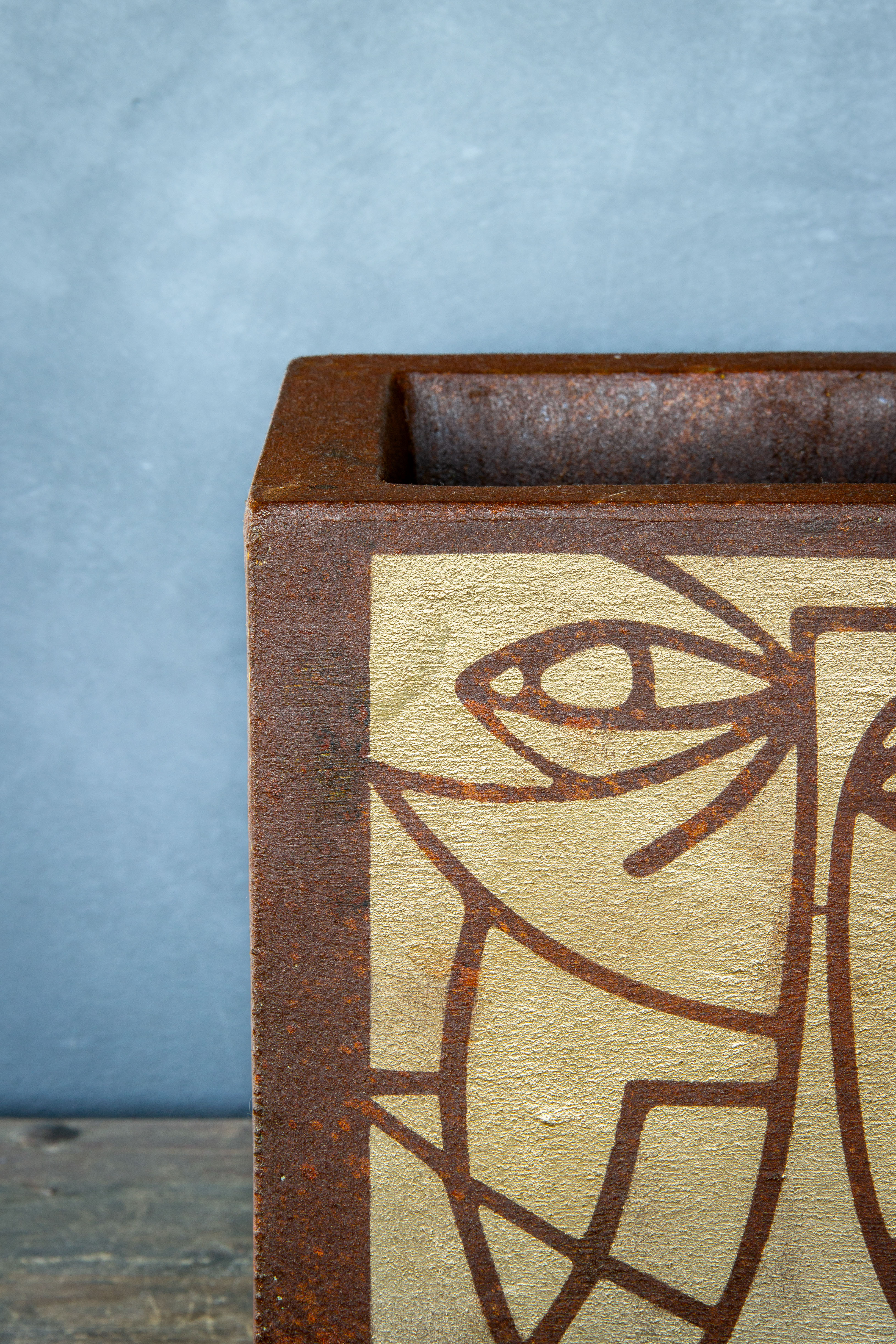 Kwadratowa osłonka loft w efekcie kortenu z ręcznie malowaną, złotą geometryczną twarzą